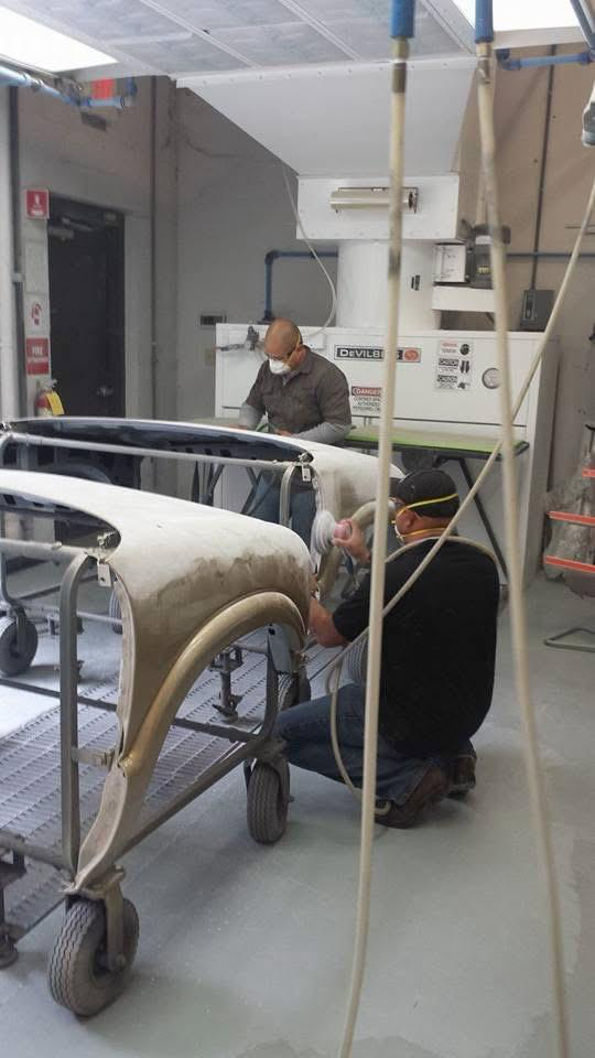 Technicians sanding and shaping a vehicle body panel inside the shop